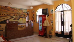 A reception area with a wooden counter, a Coca-Cola refrigerator, a clock, and a mural on the wall. - Hostal Tambo Colorado (Pisco)