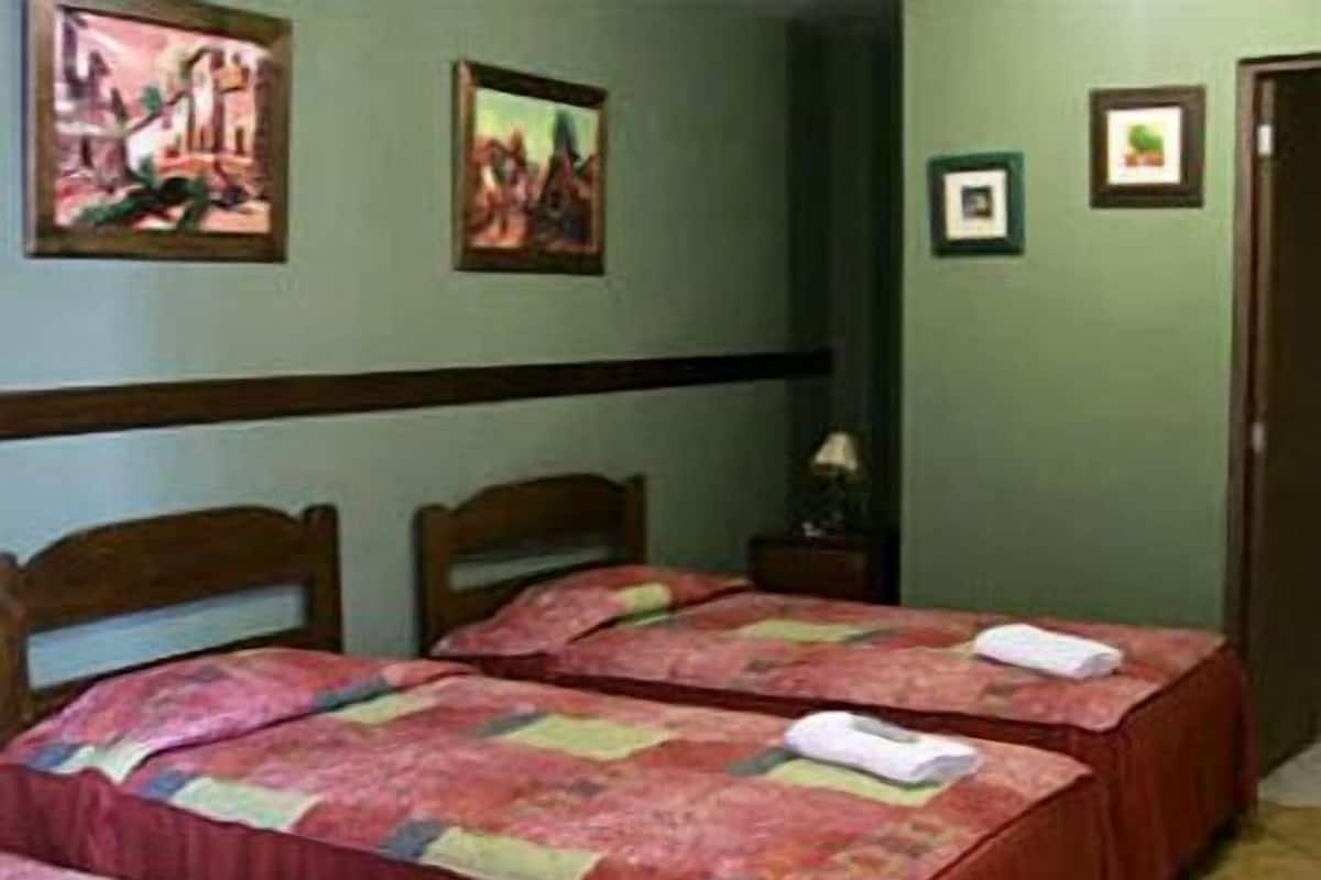 A hotel room with two single beds, a nightstand, and a door.