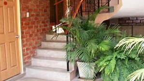 A staircase with a wooden handrail, a brick wall, and potted plants. - Hostal Tambo Colorado (Pisco)