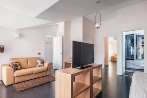Ein modernes Wohnzimmer mit Sofa, Fernseher und Holzkonsole, das in ein Badezimmer mit Badewanne und Dusche übergeht.