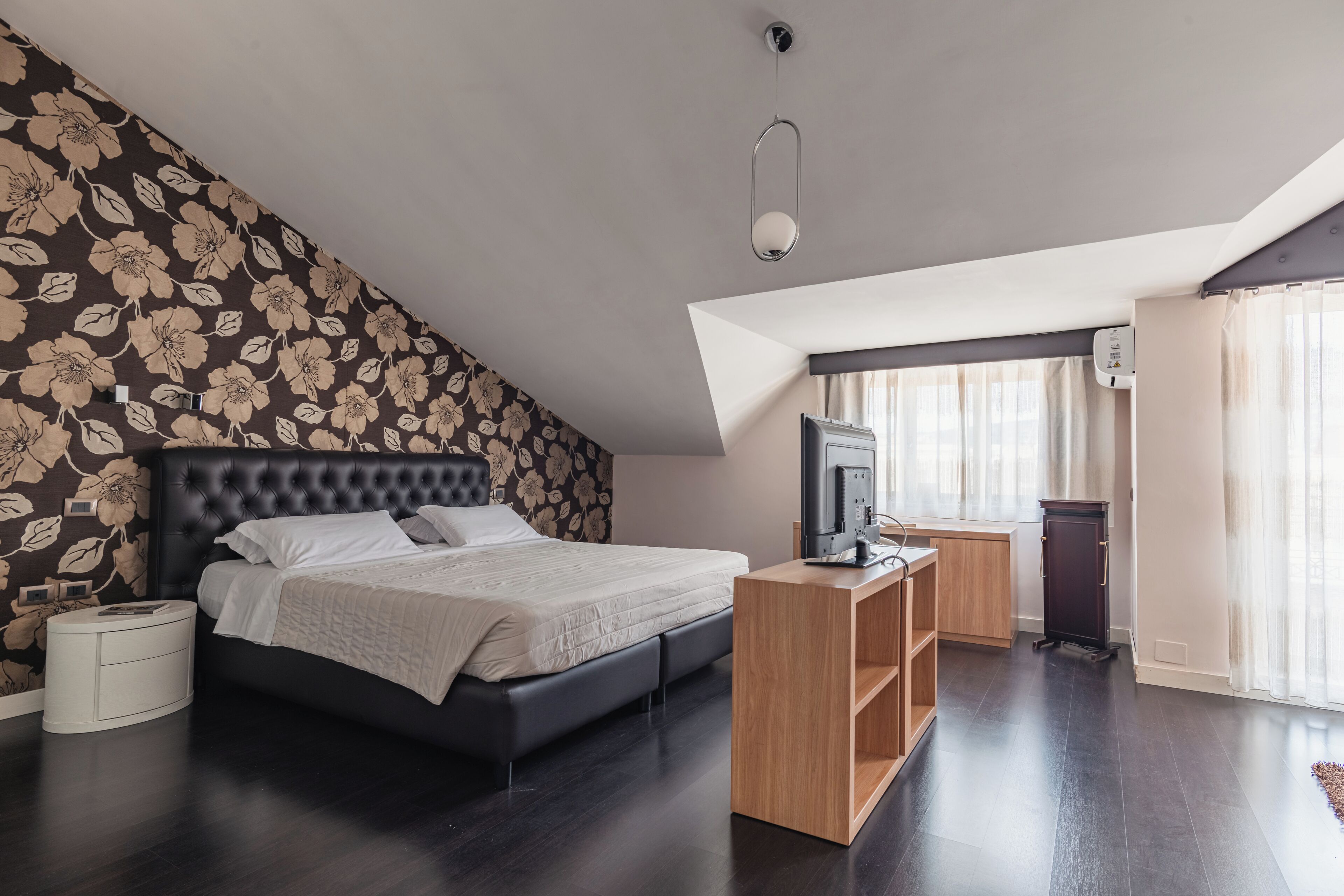 A modern bedroom with a large bed, a TV, a wooden desk, and a dark floor.