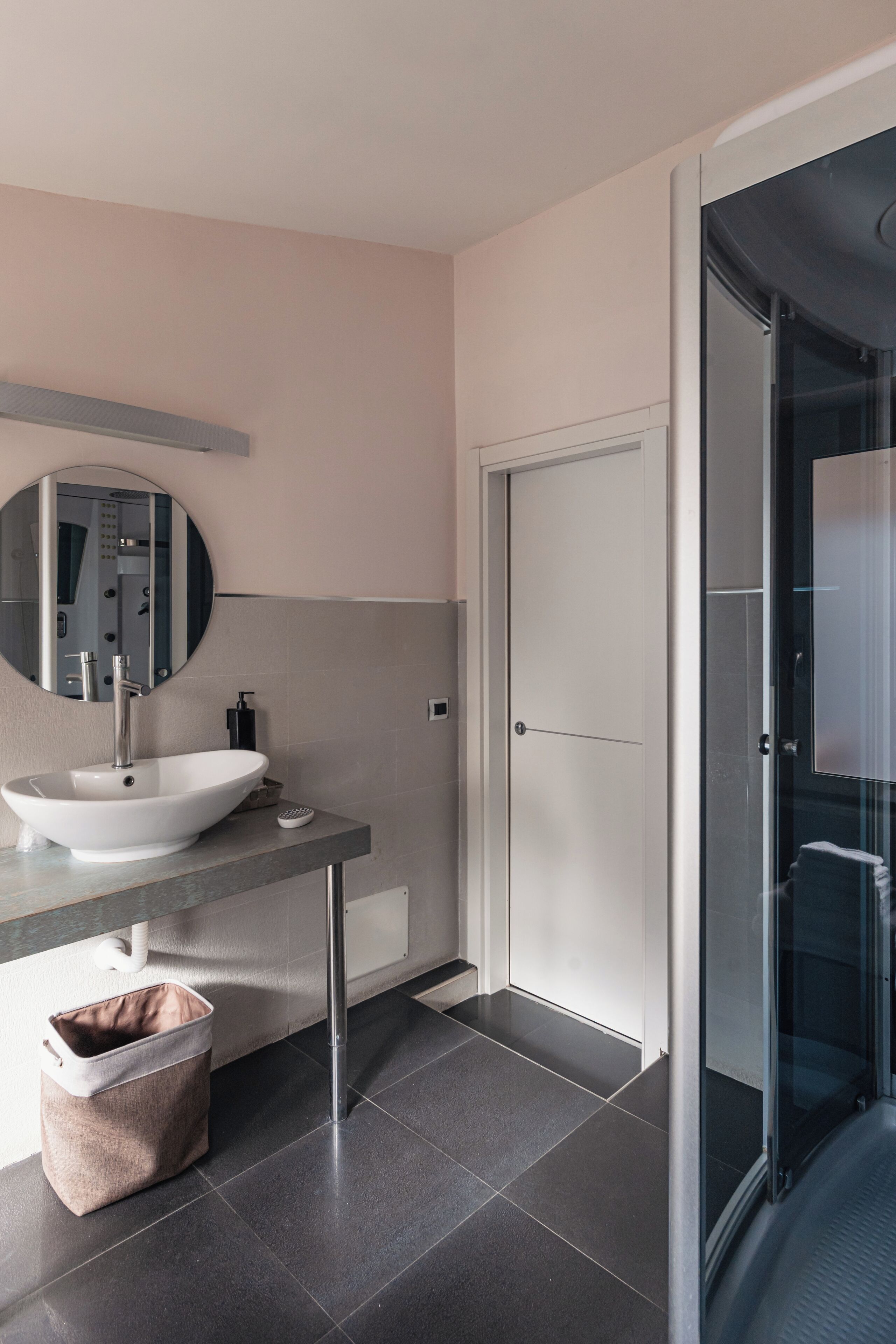 Une salle de bain moderne avec un miroir rond, un lavabo blanc et une cabine de douche en verre.