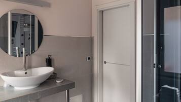 Une salle de bain moderne avec un miroir rond, un lavabo blanc et une cabine de douche en verre.