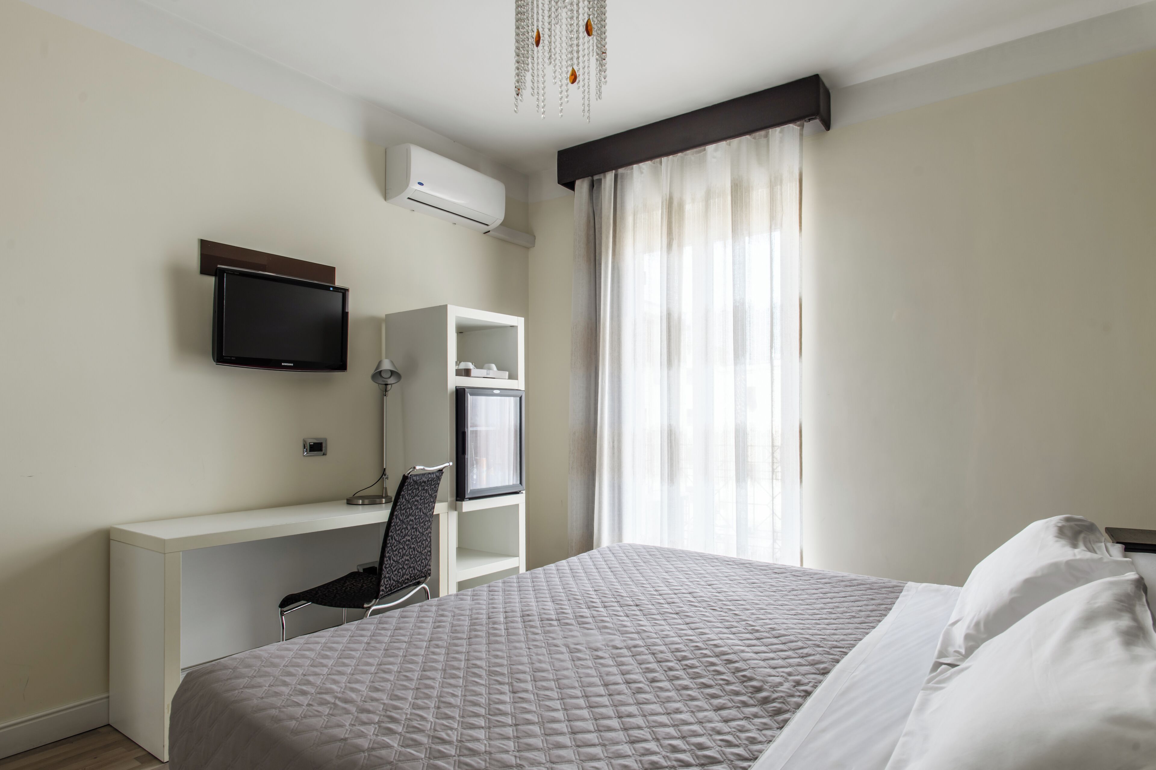 Una habitación de hotel con cama, escritorio con silla, televisor y aire acondicionado.
