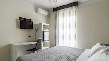 Una habitación de hotel con cama, escritorio con silla, televisor y aire acondicionado.