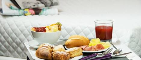 Un plateau de petit-déjeuner avec des viennoiseries, des fruits et un verre de jus, posé sur une table blanche.