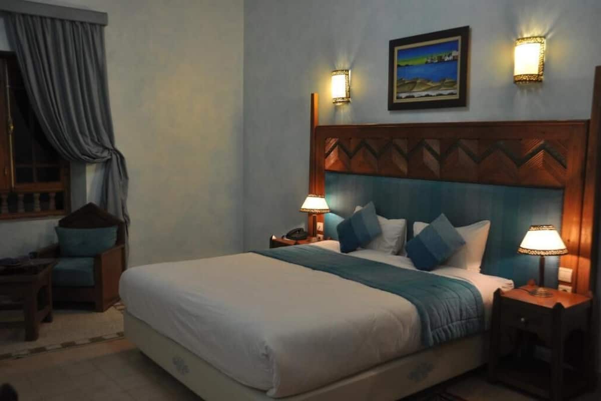 A hotel room with a large bed, two bedside lamps, a nightstand, a chair, and a window with curtains.