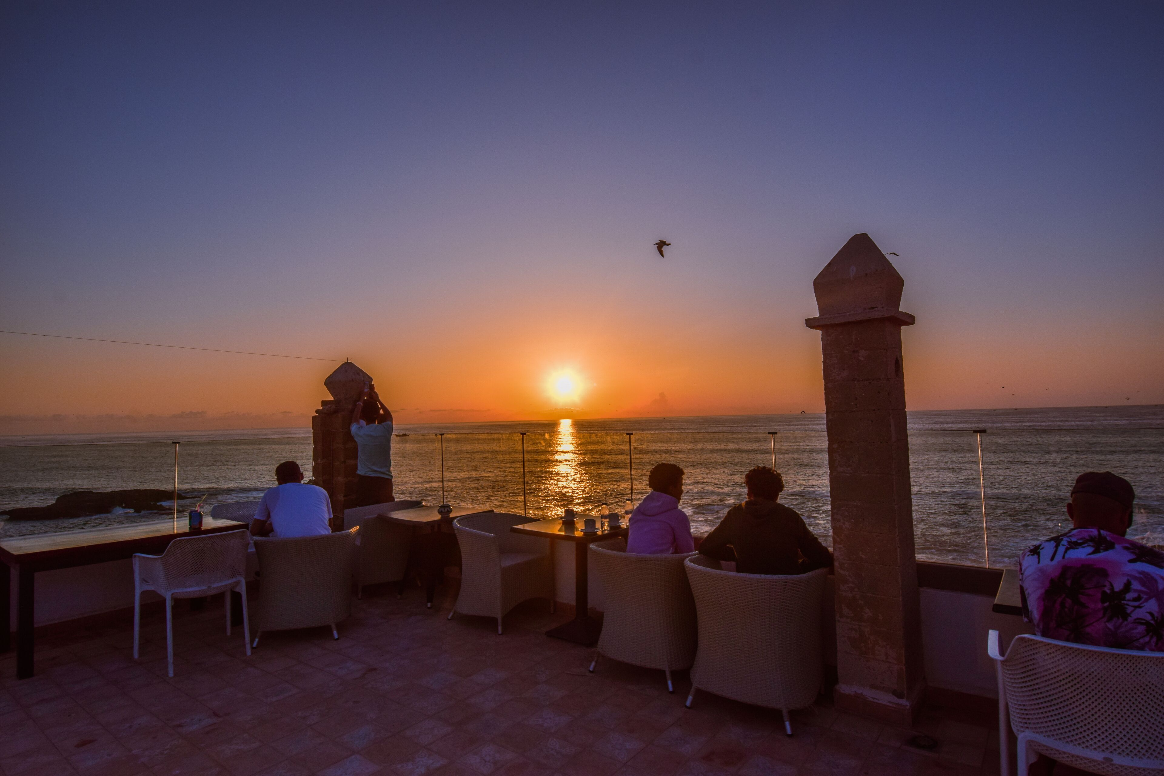 Blick auf den Sonnenuntergang von einer Sitzterrasse mit Tisch und Stühlen, mit Blick auf das Meer.
