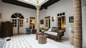 Un interior espacioso con un techo alto, una zona de estar central con un sofá y sillones, y una gran columna en el centro.