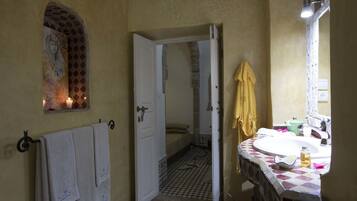 A bathroom with a tiled floor, a sink with a mirror, a towel rack, and a door leading to another room.
