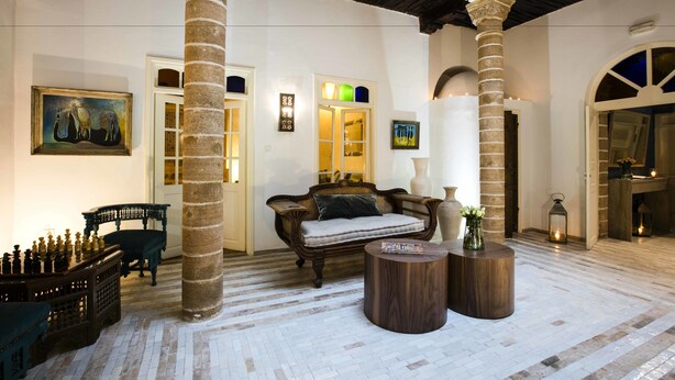 Un hall d’entrée spacieux avec un plafond haut, de grandes colonnes, un coin salon confortable et un échiquier peint sur le sol.