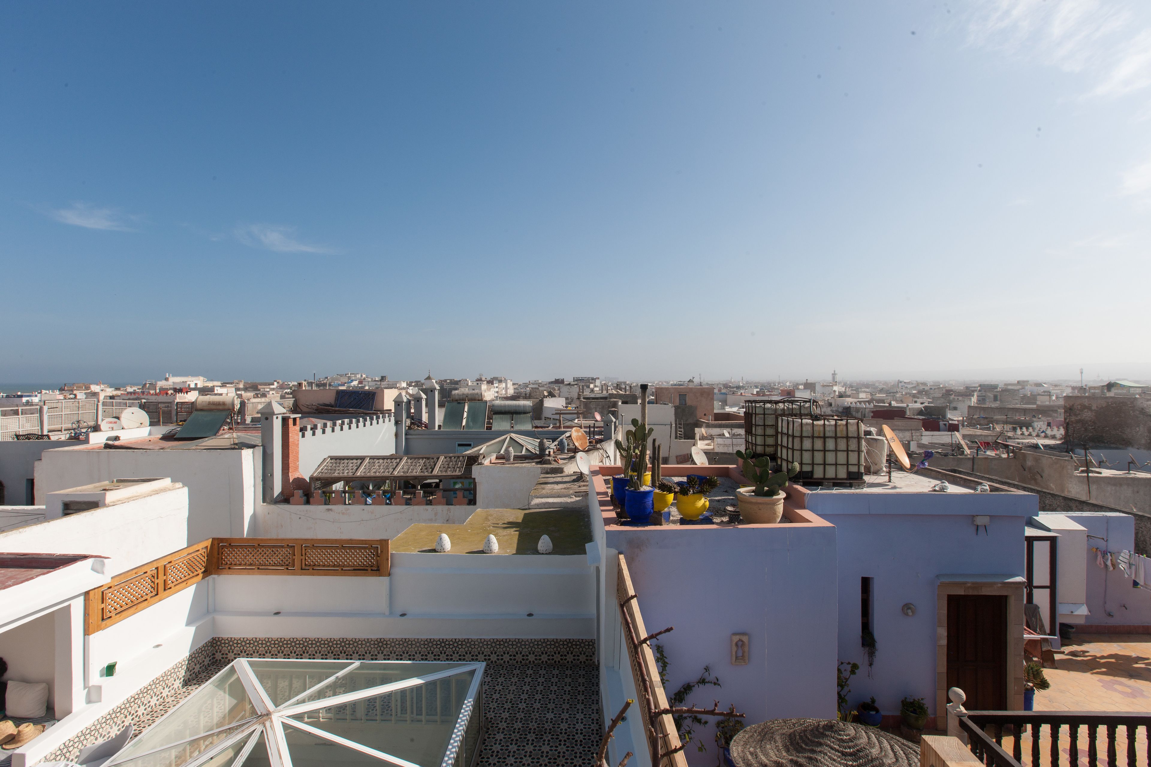 A rooftop terrace with a glass balustrade, potted plants, and a view of the cityscape.