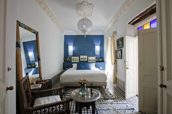 A hotel room with a large bed, a sitting area with a chair, a small table with a vase, and a decorative ceiling light.