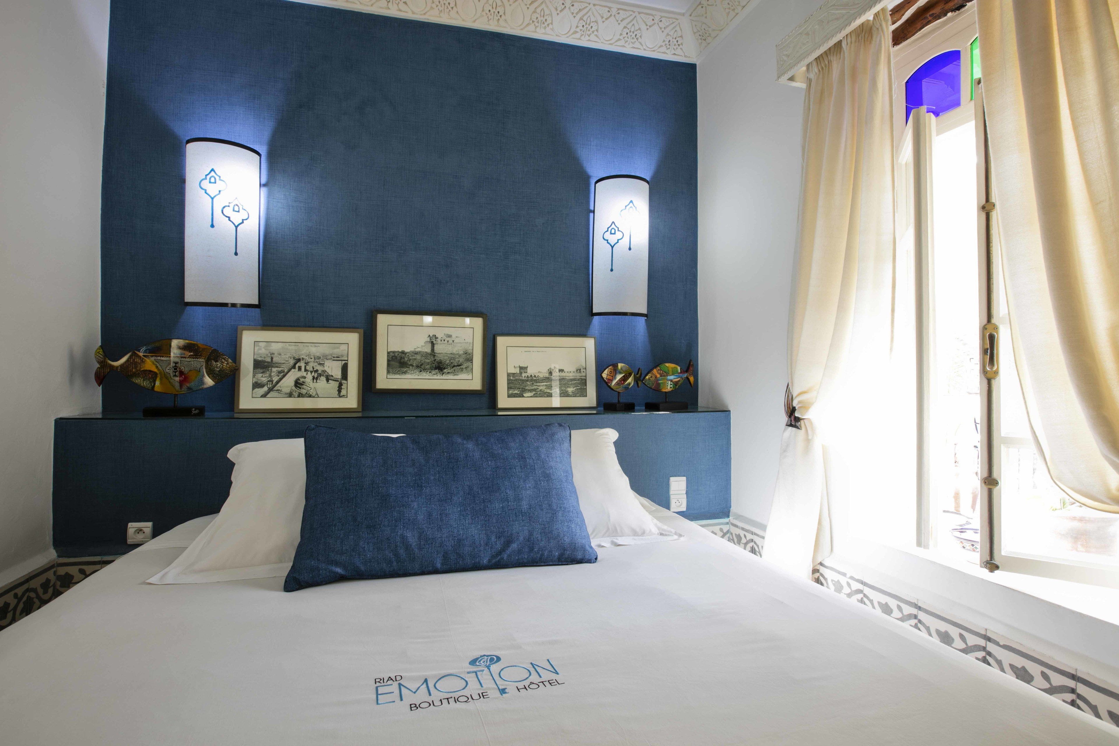 Una habitación de hotel con una cama, cuadros en la pared y una ventana con cortinas.