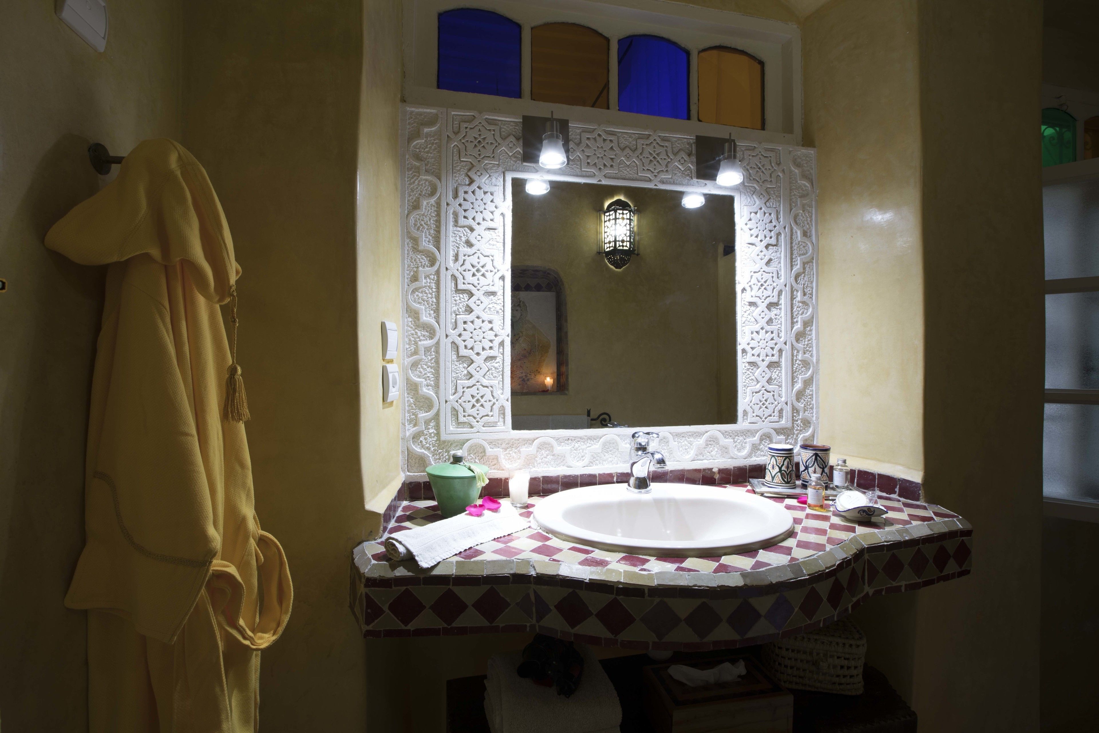Ein Badezimmer mit einem weißen Waschbecken, einem Spiegel mit dekorativem Rahmen und einem Handtuch an der Wand.