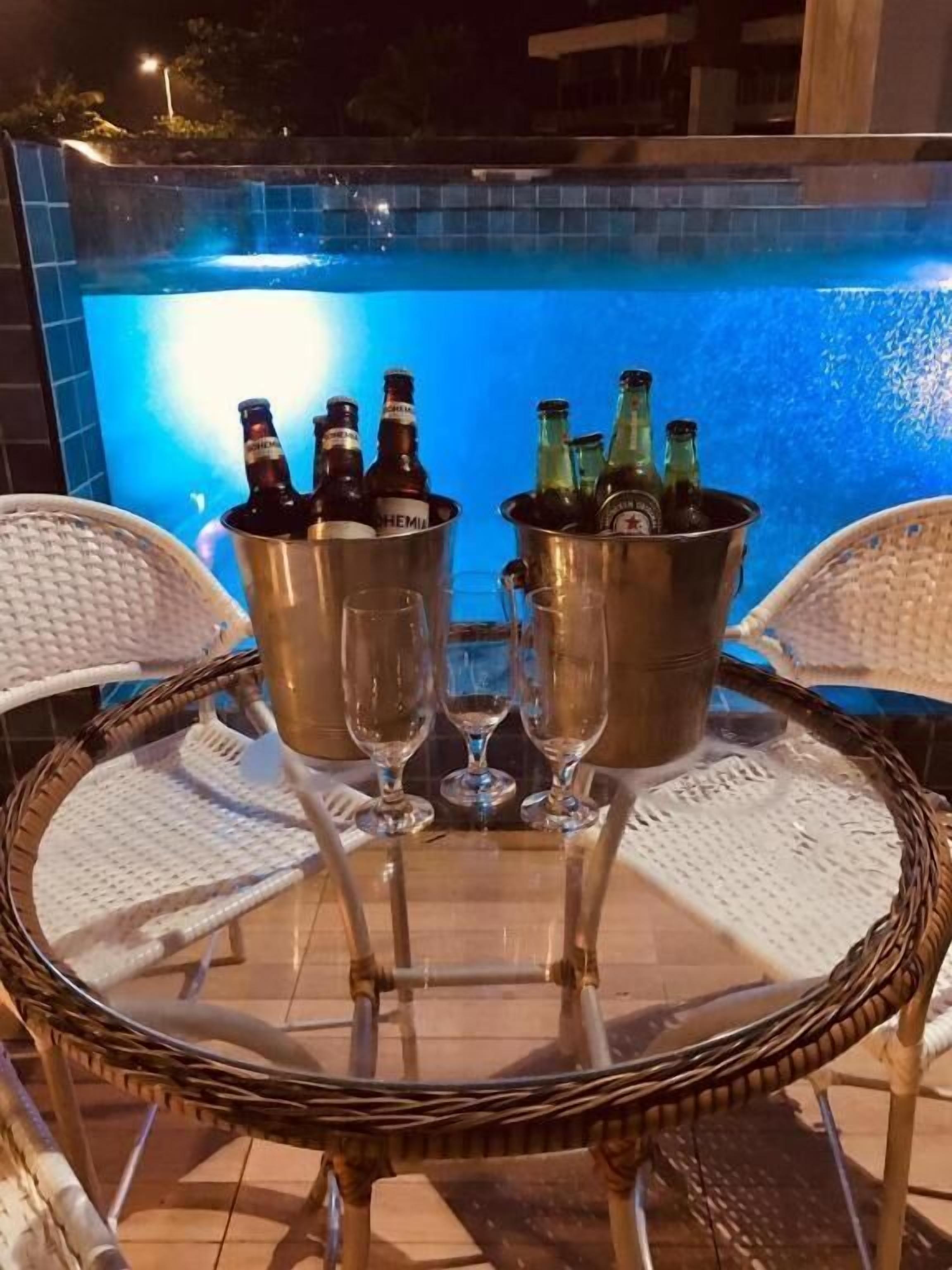 Ein Tisch am Pool mit zwei Metalleimern, die Flaschen und Gläser enthalten, umgeben von Korbstühlen.