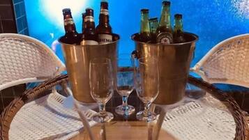 Ein Tisch am Pool mit zwei Metalleimern, die Flaschen und Gläser enthalten, umgeben von Korbstühlen.