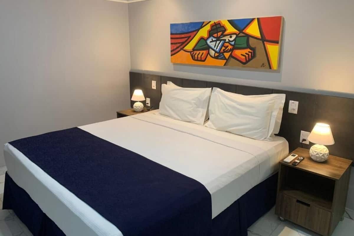 A hotel room with a large bed, two bedside tables, a nightstand, and a colorful abstract painting on the wall.