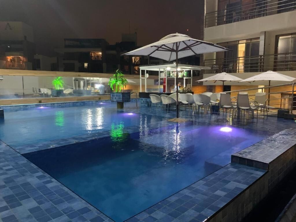 Una piscina interior con suelo de baldosas, sillas de descanso, sombrillas y una zona de bar.