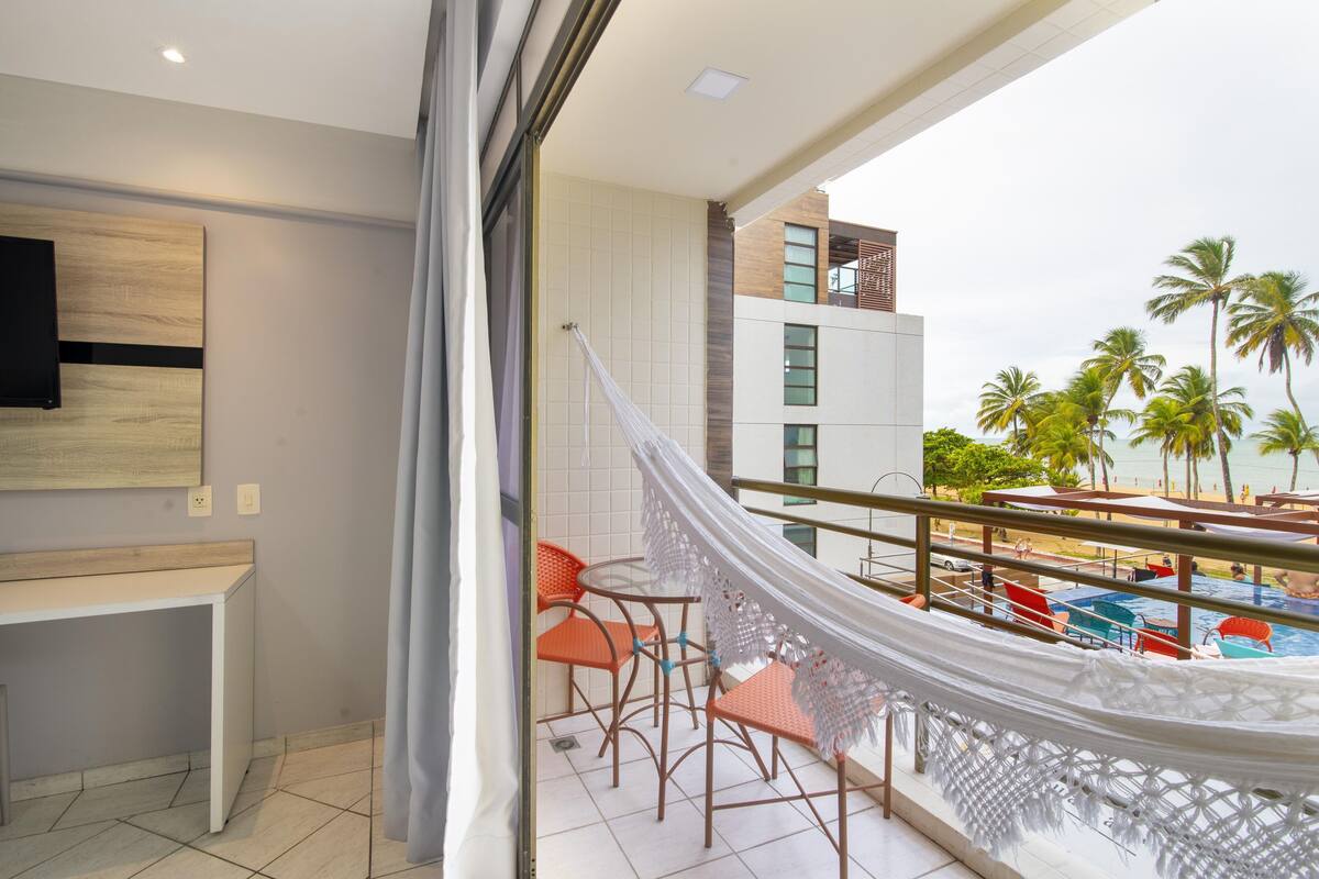 A balcony with a hammock, a pool, and a view of palm trees.