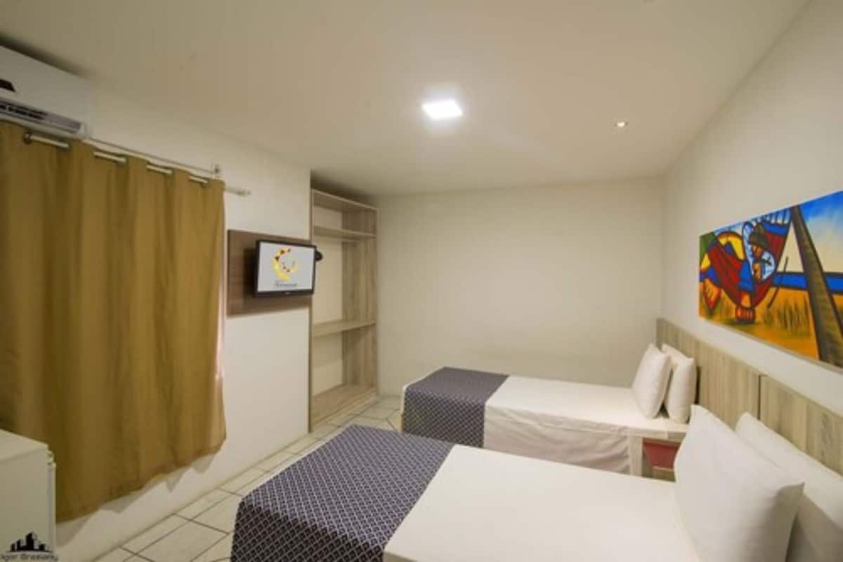 A hotel room with two beds, a TV, a painting, and a shower curtain.
