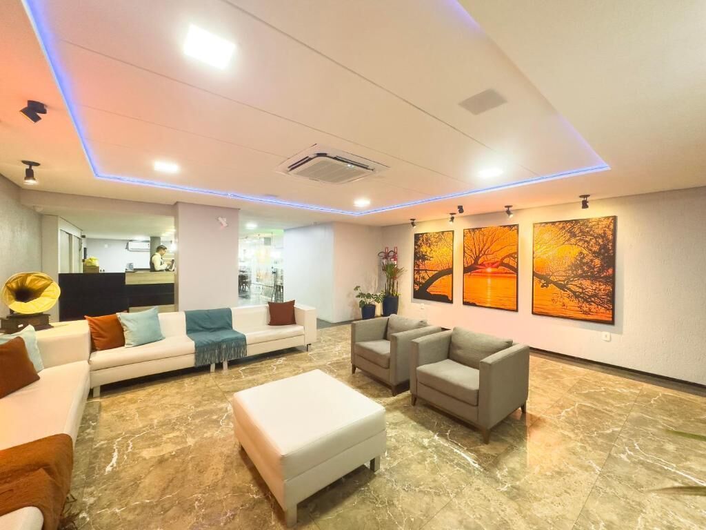 A modern lobby with a white sofa, armchairs, and a coffee table. There are three paintings on the wall and a plant.