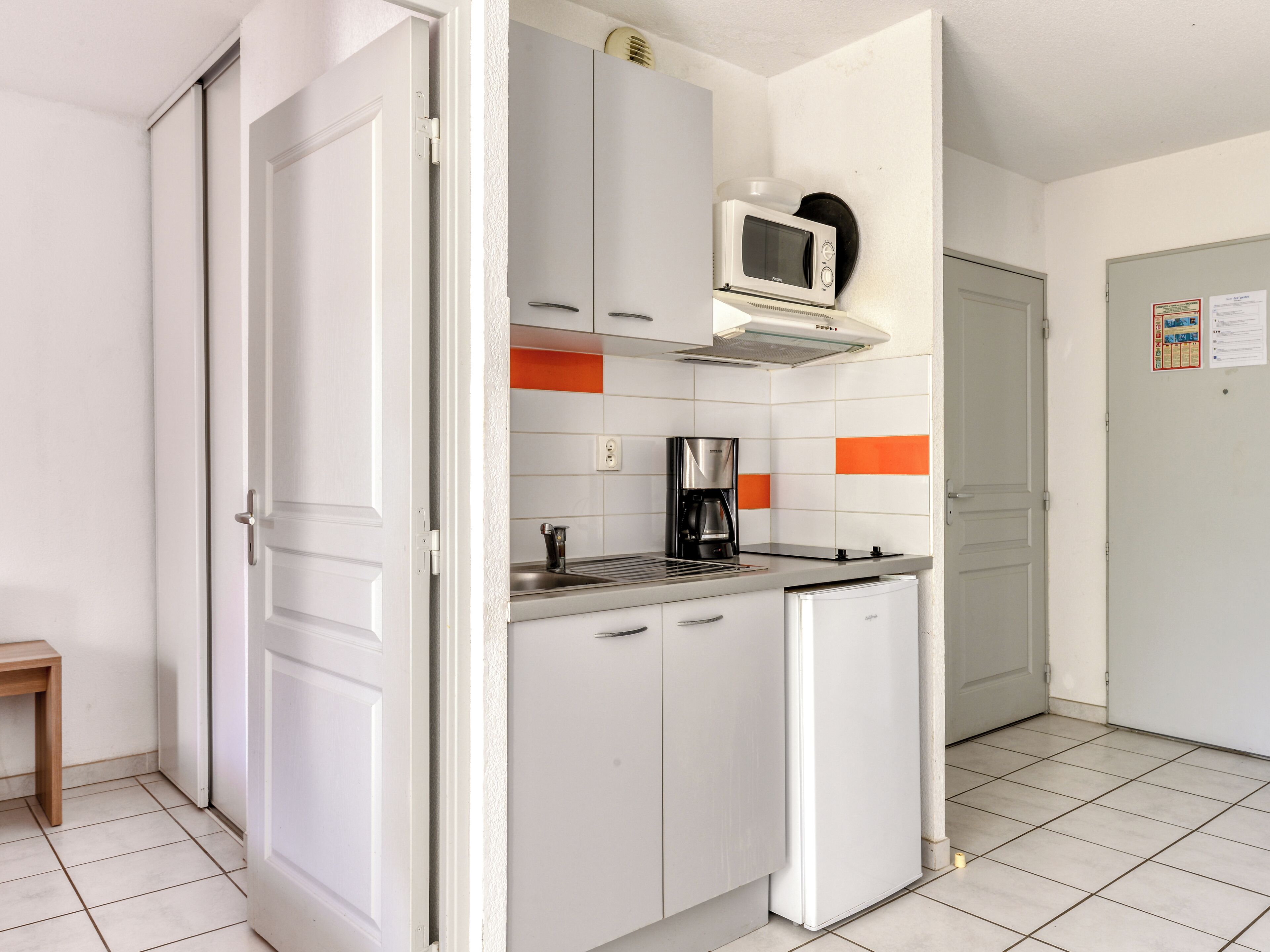 A compact kitchen with white cabinets, a microwave, a coffee maker, and a small refrigerator.