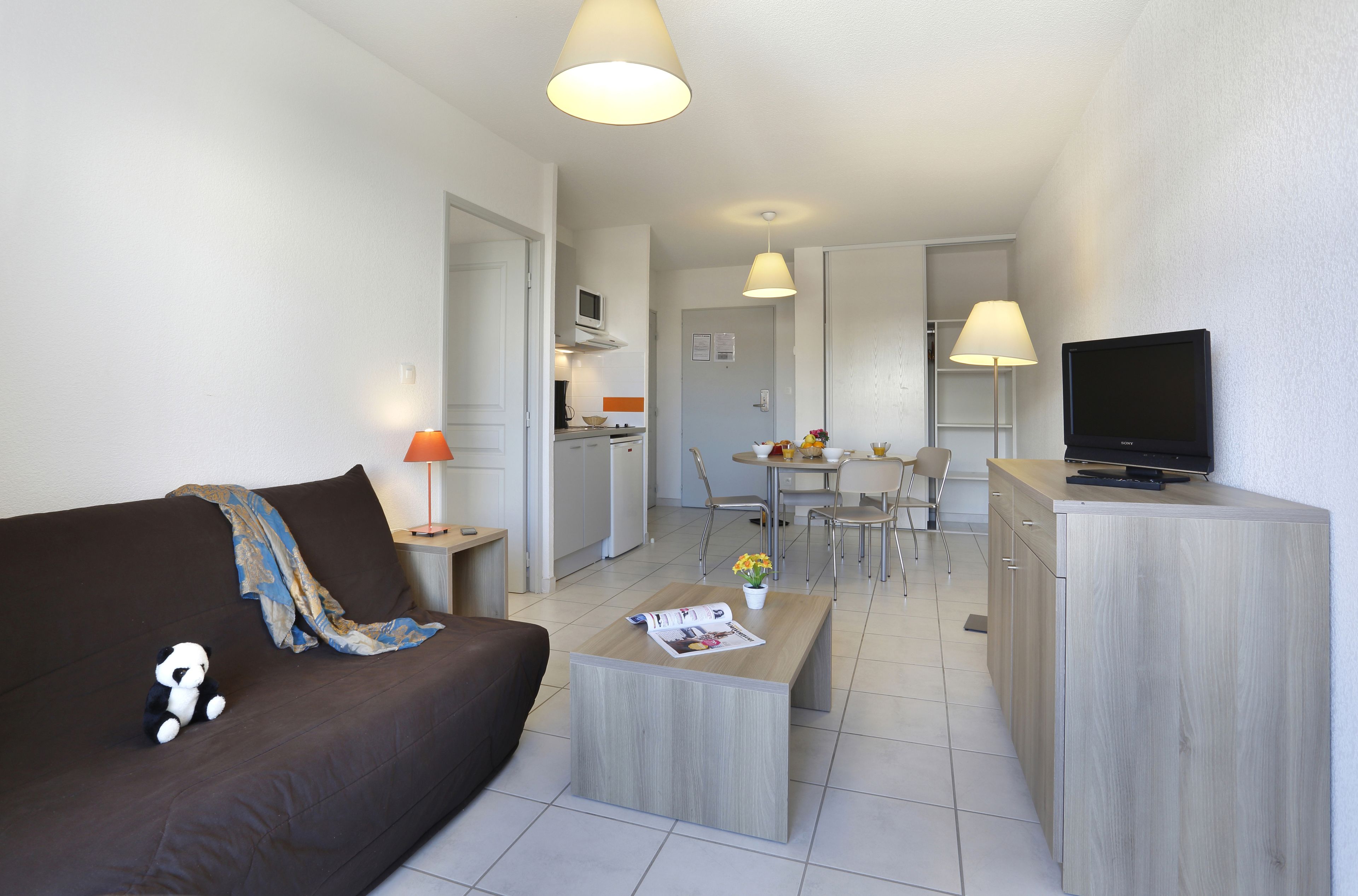 A modern living room with a sofa, a coffee table, a TV, and a dining area with chairs and a table.