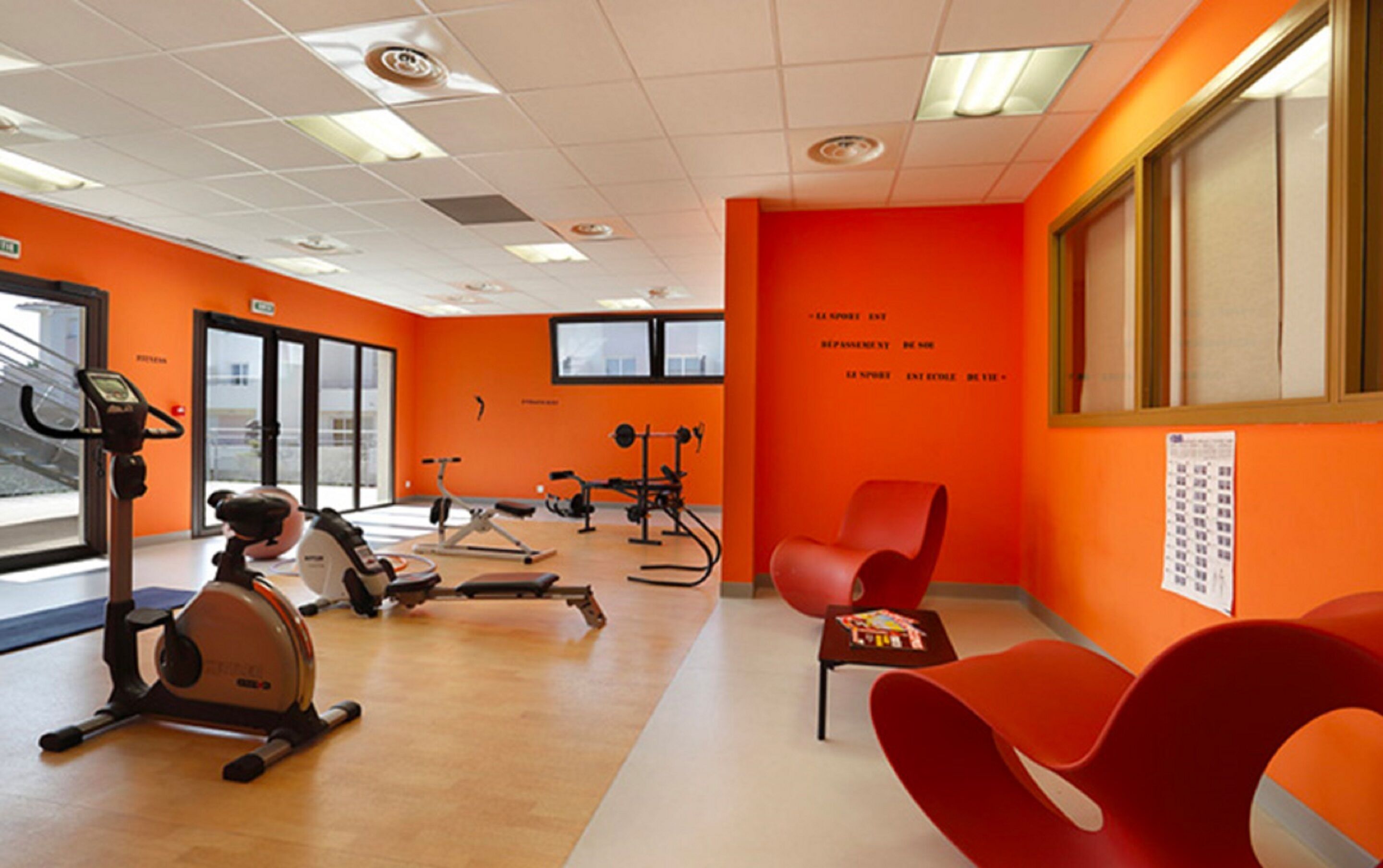 Een sportschool met oranje wanden, fitnessapparatuur en een groot raam.