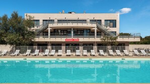 A modern building with a swimming pool in front, featuring a restaurant sign, multiple balconies, and sun loungers. - Vacancéole - Cap Camargue (Le Grau-Du-Roi)
