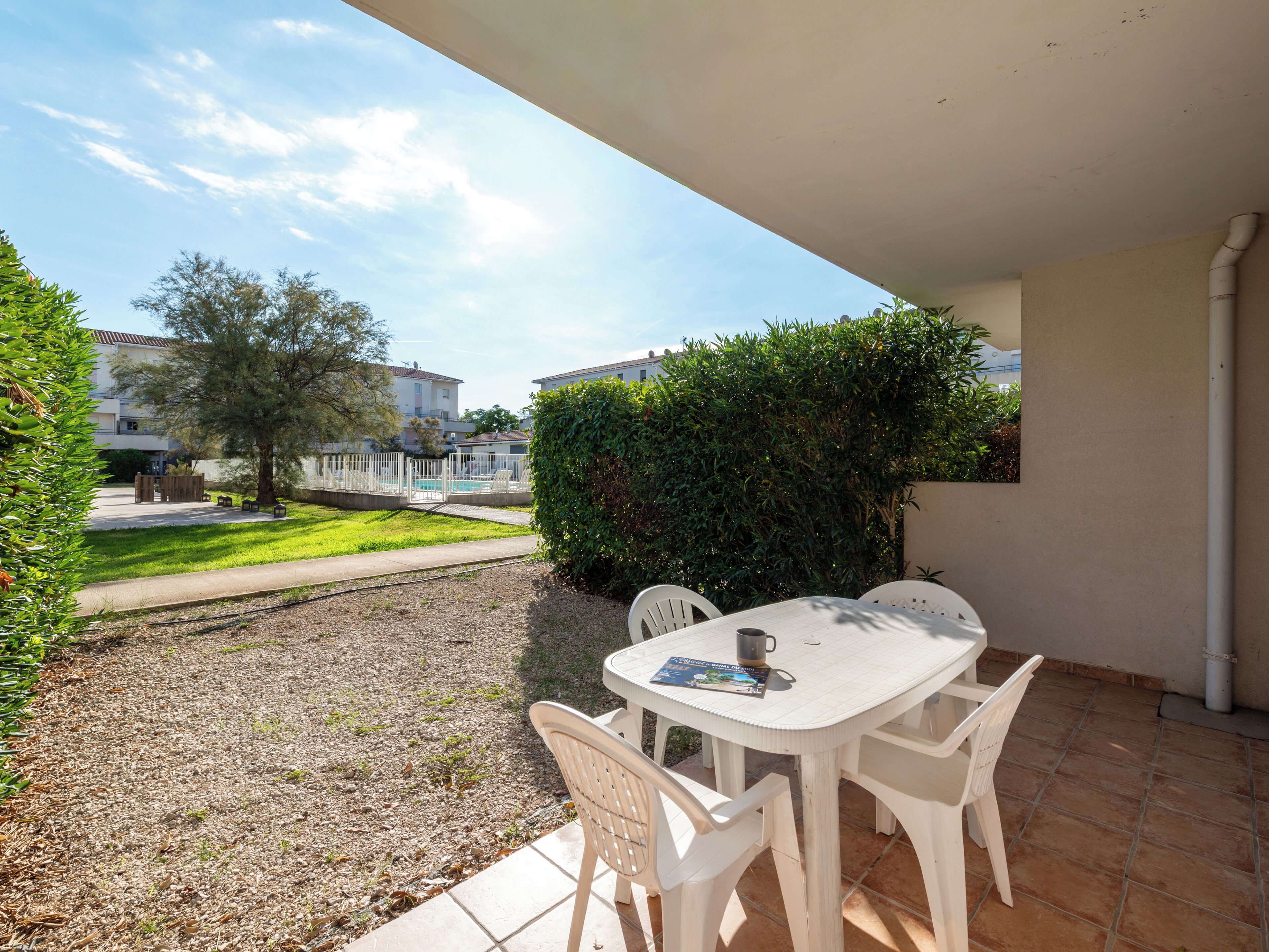 A patio with a white table and chairs, a small pool, and a view of houses and greenery.