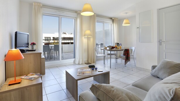 A modern hotel room with a sofa, a coffee table, a TV, and a dining area with a table and chairs. - Vacancéole - Cap Camargue (Le Grau-Du-Roi)