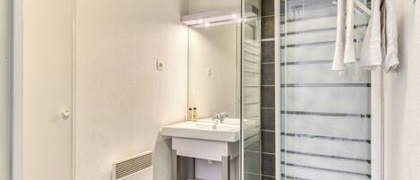 Un baño moderno con cabina de ducha de vidrio, un lavabo blanco y un perchero para toallas.