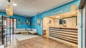 A reception area with a blue wall, a reception desk, a sofa, and hanging wicker lamps. - Vacancéole - Cap Camargue (Le Grau-Du-Roi)