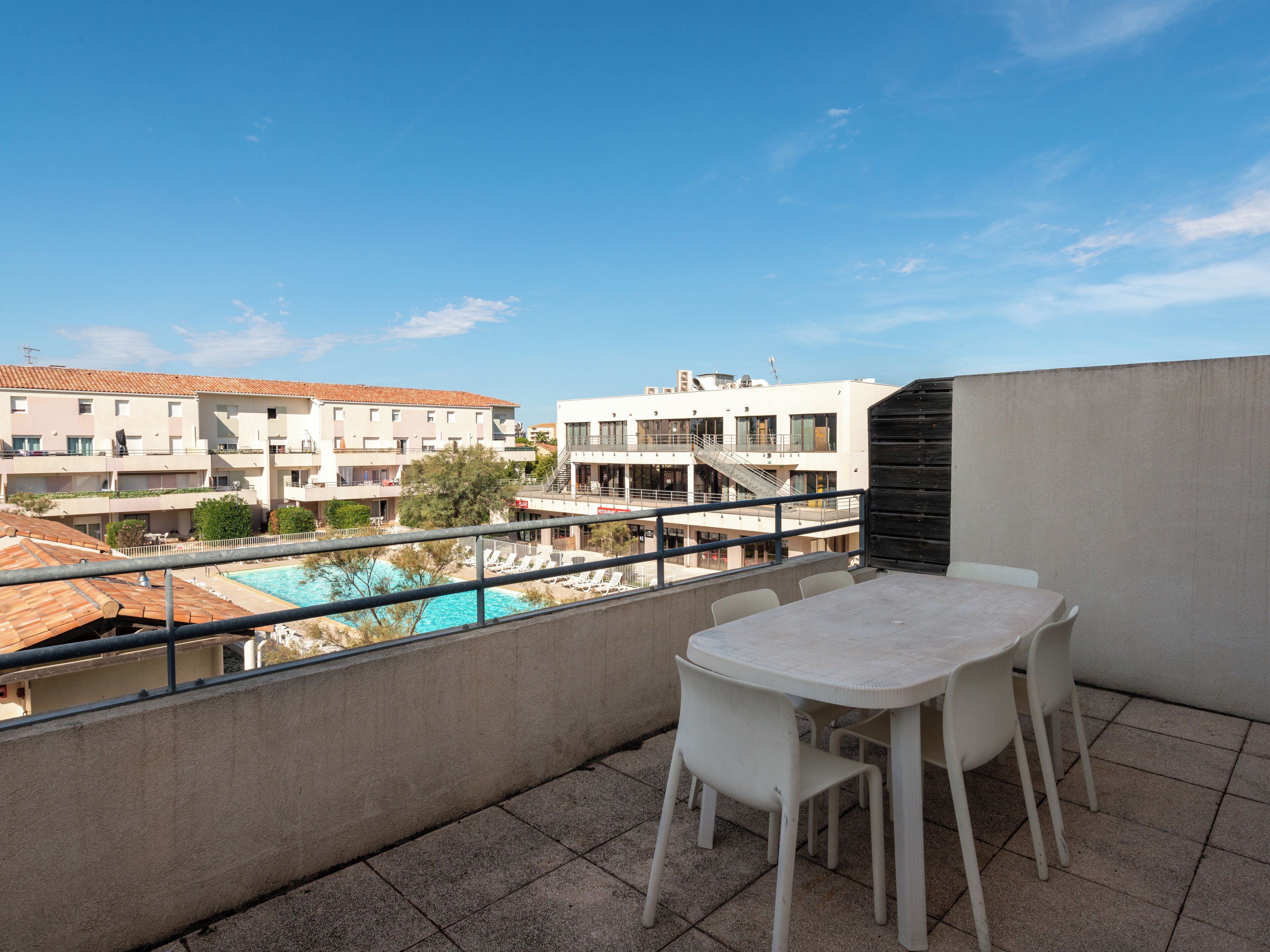 A balcony with a table and chairs overlooking a swimming pool and buildings.