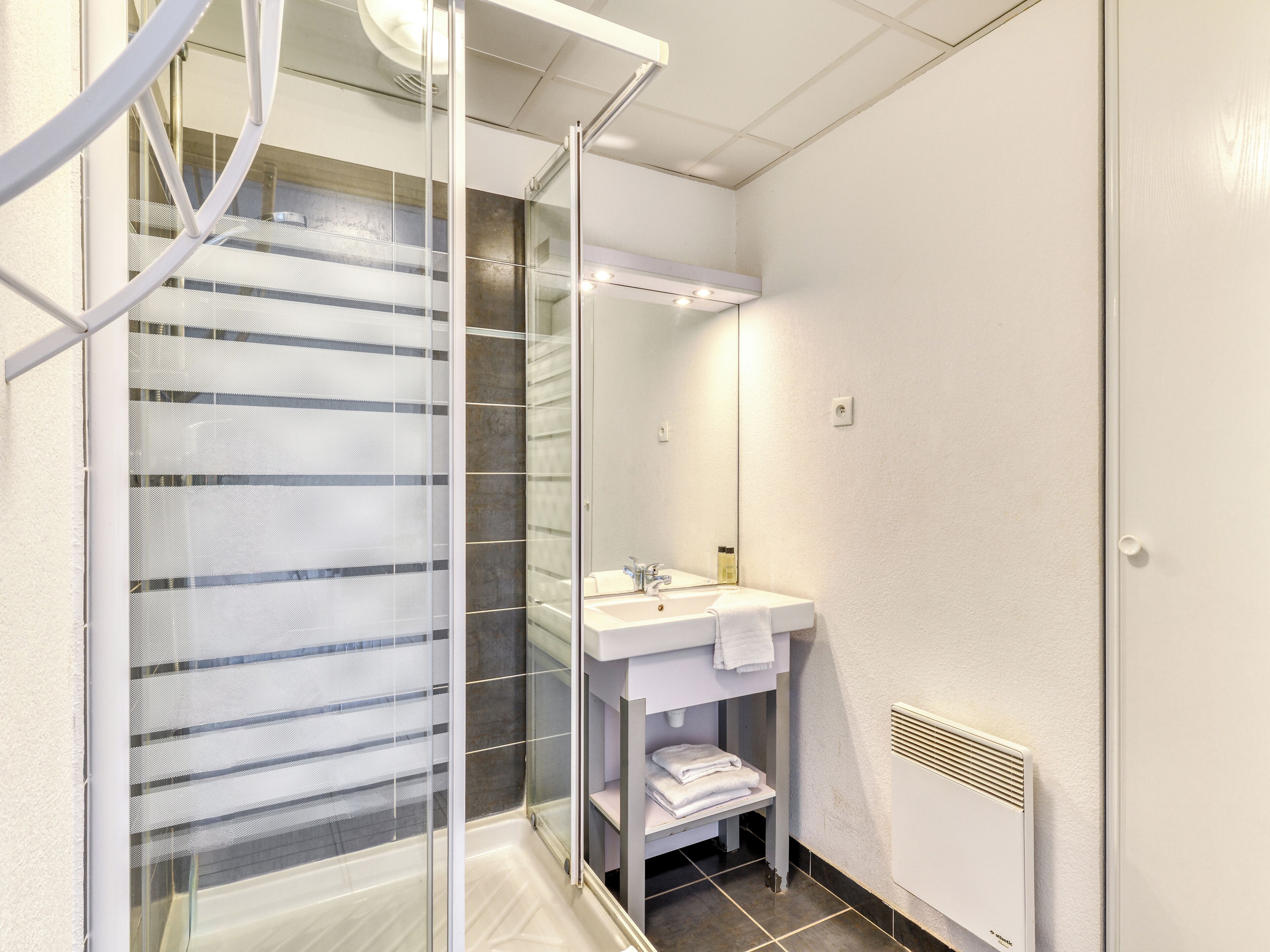 Une salle de bain moderne avec une douche à parois de verre, un lavabo avec un miroir et un porte-serviettes.