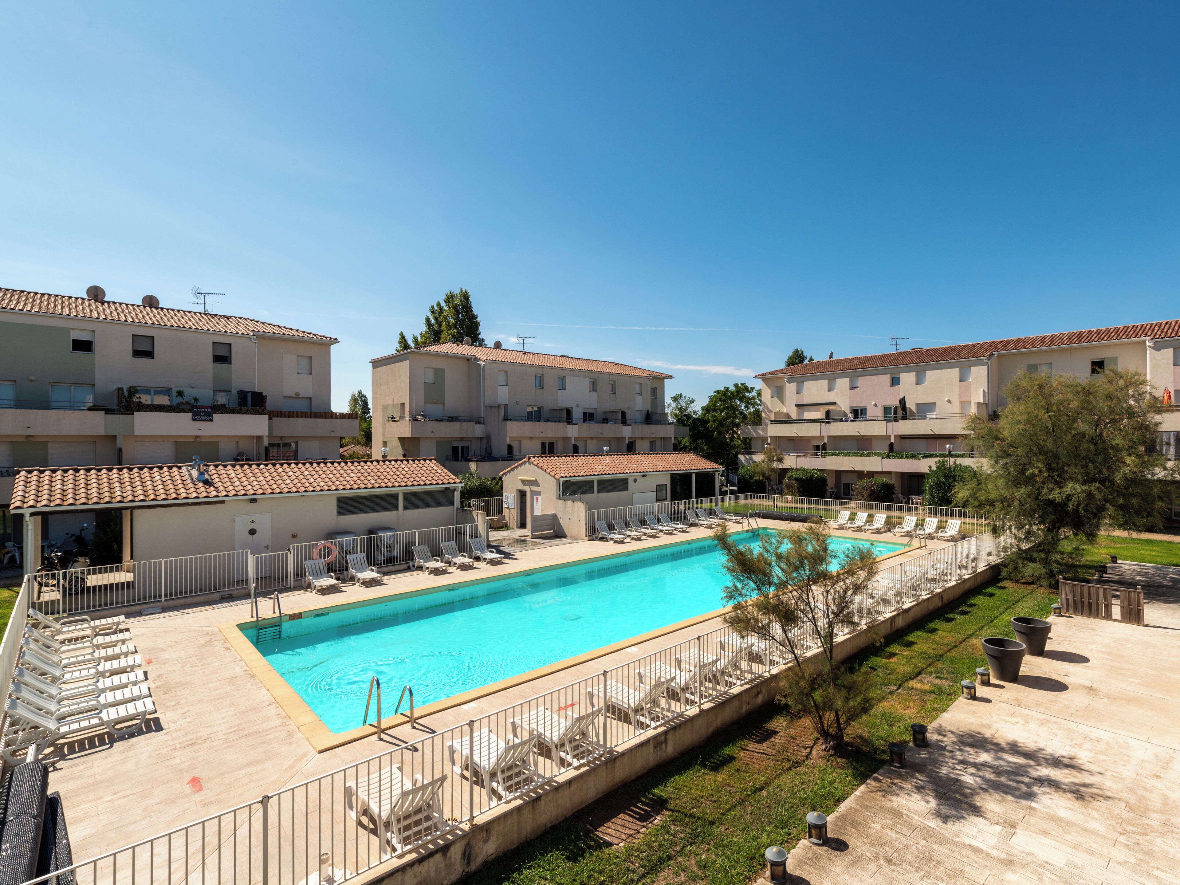 Une piscine entourée de chaises longues et un bâtiment doté d’un toit en tuiles.