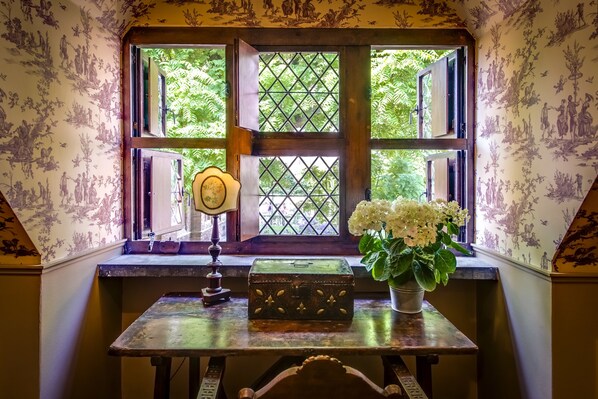 A room with a window, a table, a lamp, a vase with flowers, and a decorative box.