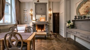 A room with a fireplace, wooden herringbone floor, a dining table with chairs, and a bench.