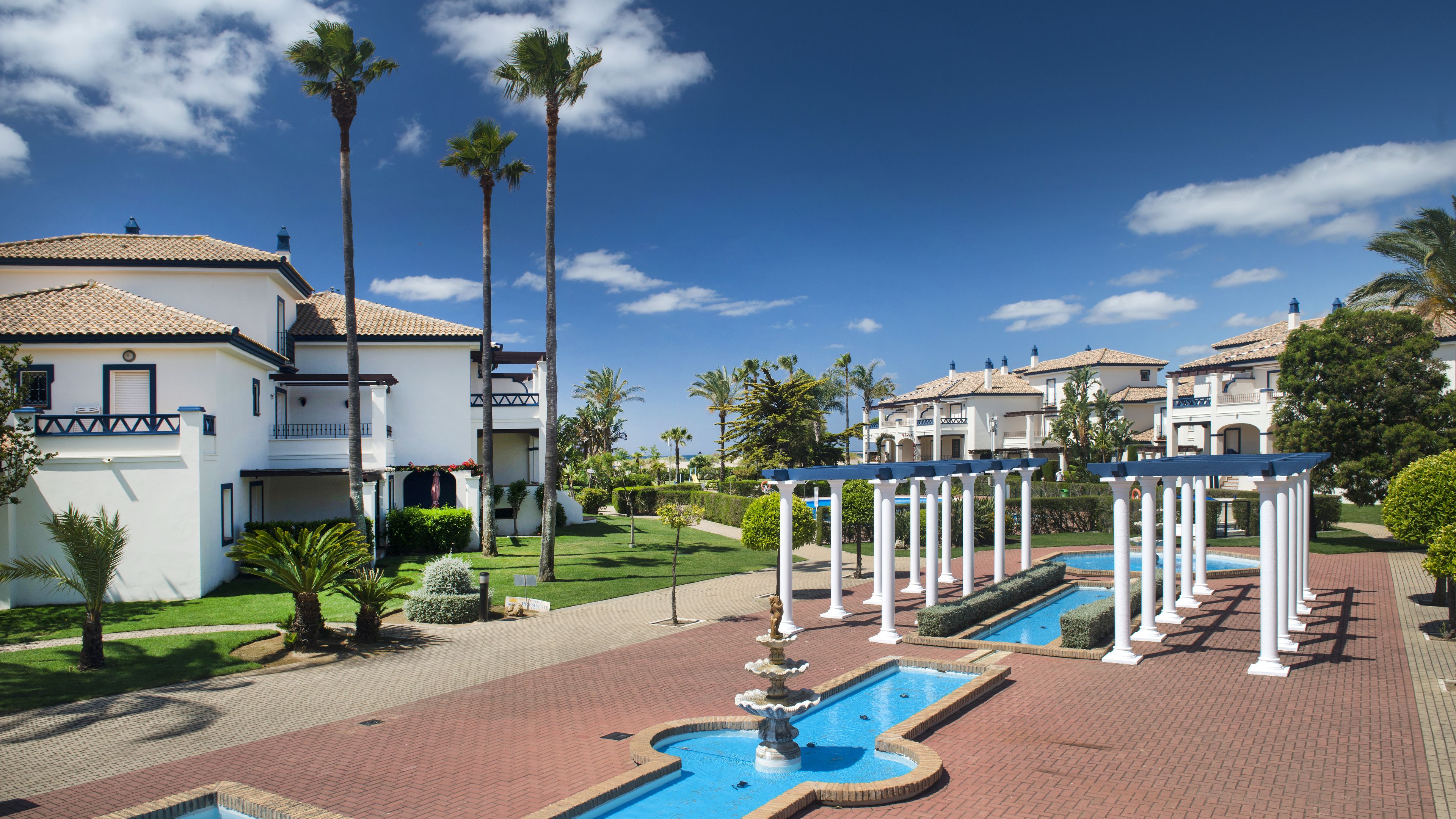 A resort with multiple white buildings, a swimming pool, and palm trees.