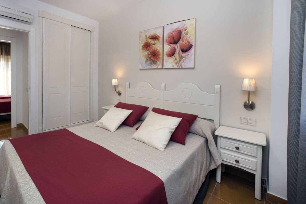 Een hotelkamer met een bed, twee nachtkastjes, een kledingkast en een schilderij aan de muur.