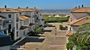 A coastal residential area with terracotta-tiled buildings, a paved street, and a view of the ocean. - Leo Apartamentos San Bruno (Ayamonte)