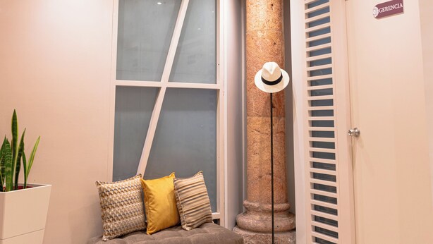 Un vestíbulo moderno con un sofá, una lámpara decorativa en el techo, un pilar y una puerta que indica “GERENCIA”.