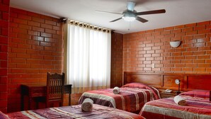 Une chambre d’hôtel avec deux lits, une tête de lit en bois, un ventilateur de plafond et un mur en briques.