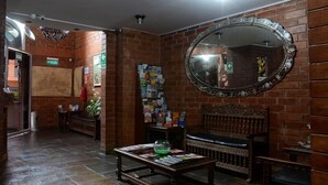 Un hall d’entrée avec un mur en briques, un grand miroir, un banc en bois et une table sur laquelle sont posés des magazines et un saladier en verre.