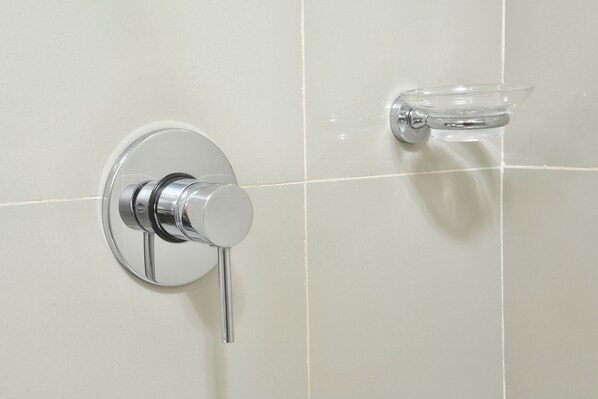 A bathroom with a chrome faucet and a clear glass soap dish mounted on the wall.