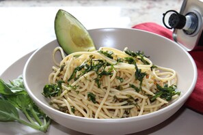 Een portie spaghetti met kruiden en een plak avocado.