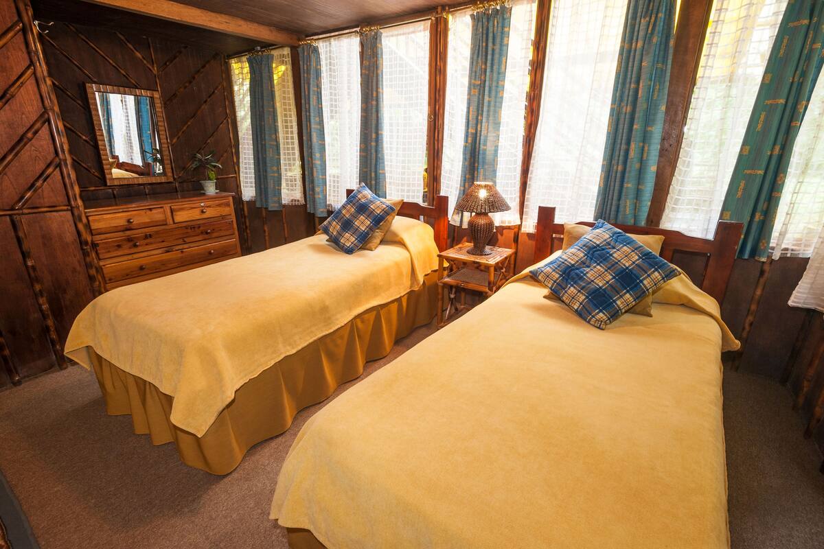 Ein Zimmer mit zwei Betten, Holzmöbeln, einem Spiegel und Vorhängen.