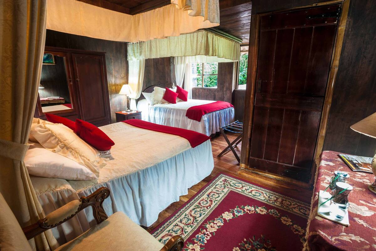 Ein traditionell eingerichtetes Zimmer mit einem Bett, einem Holzschrank, einem Nachttisch und einem Fenster mit Blick ins Grüne.