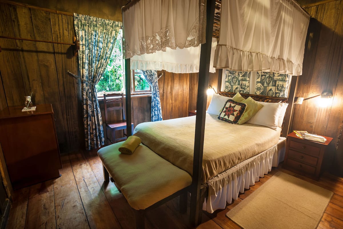 Ein Himmelbett mit Baldachin, Holzwände, ein kleiner Nachttisch und ein Fenster mit Vorhängen.